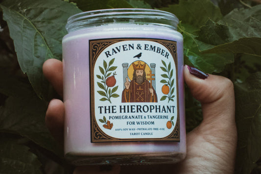 Hand holding a candle labeled 'The Hierophant' against a leafy background