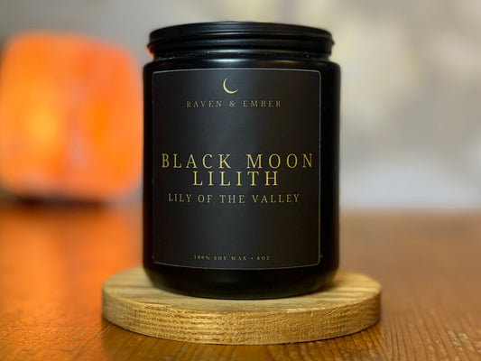 Black candle labeled 'Black Moon Lilith' on a wooden coaster with a blurred background