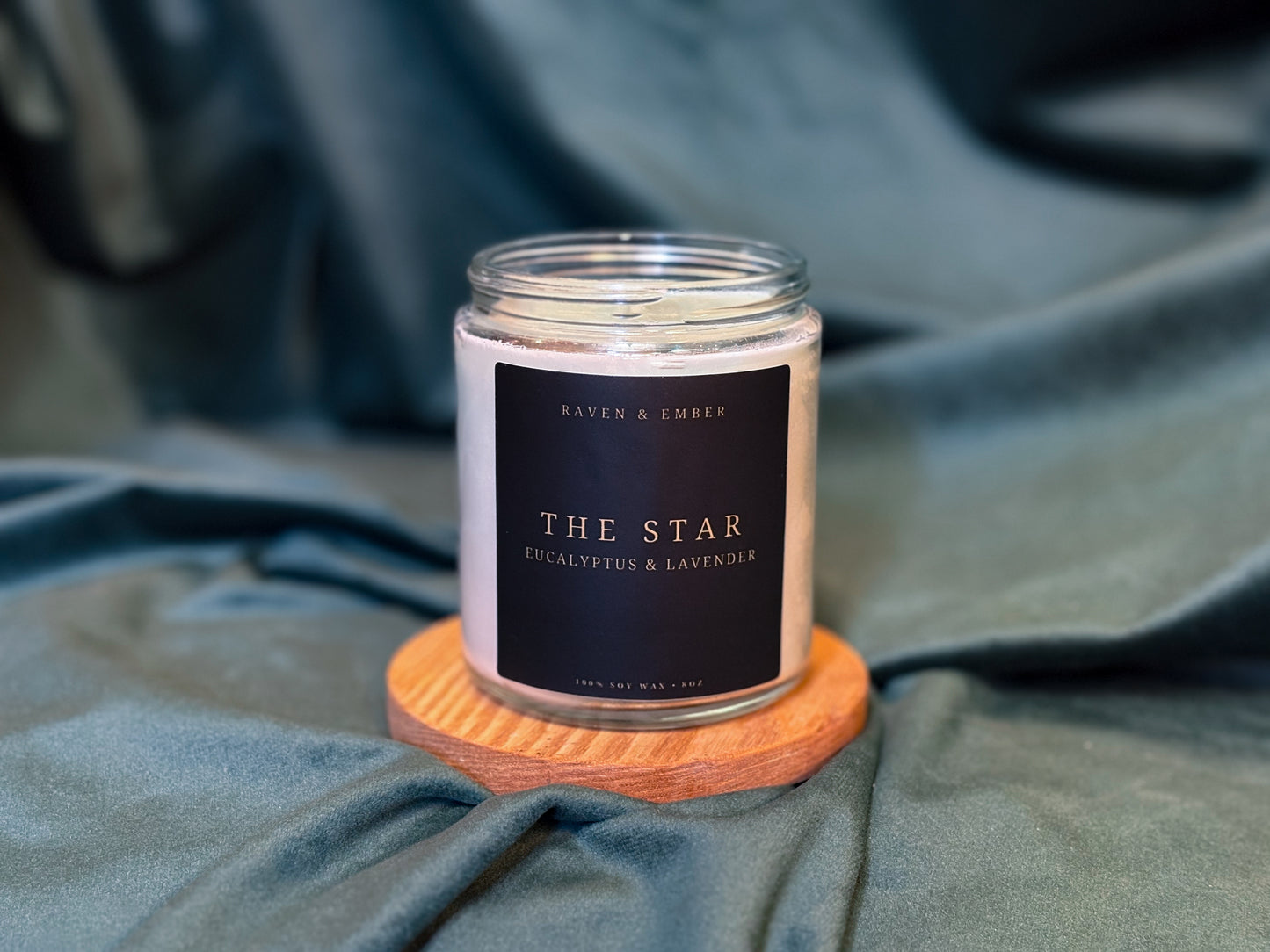 Candle labeled 'The Star' on a wooden coaster with a dark label against a textured fabric background