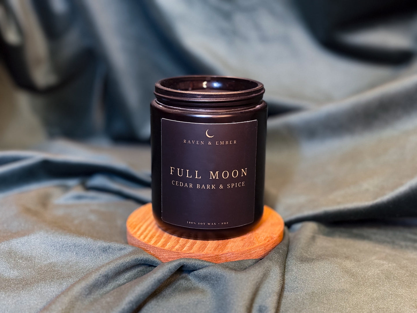 Candle labeled 'Full Moon' by Raven & Ember on a textured fabric background