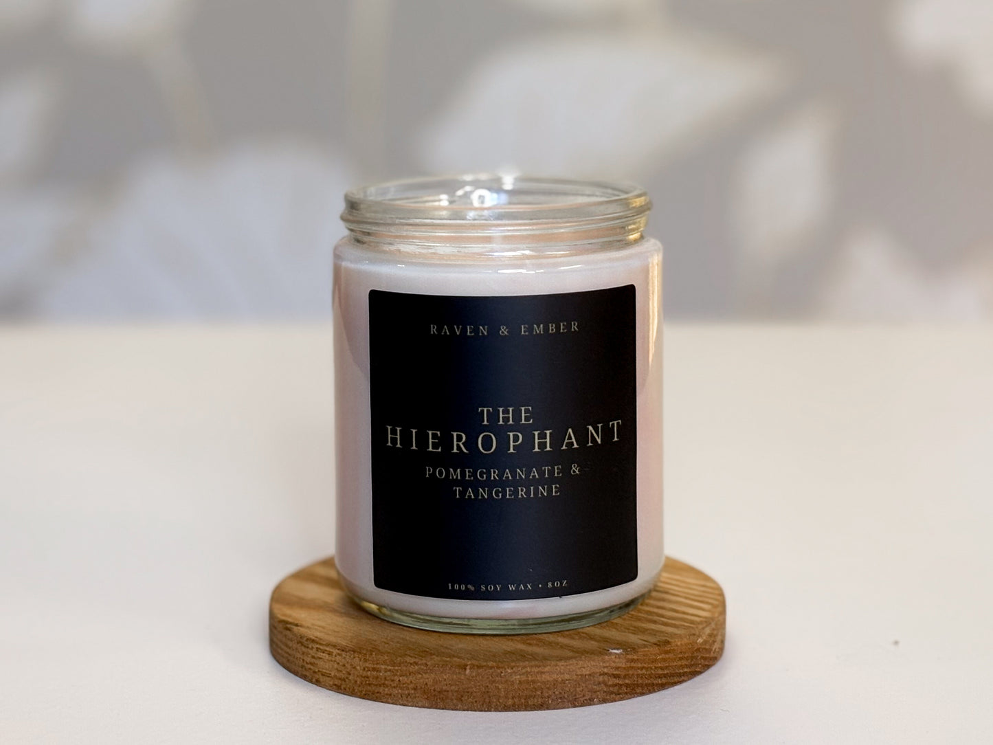 Candle with a label on a wooden coaster against a neutral background