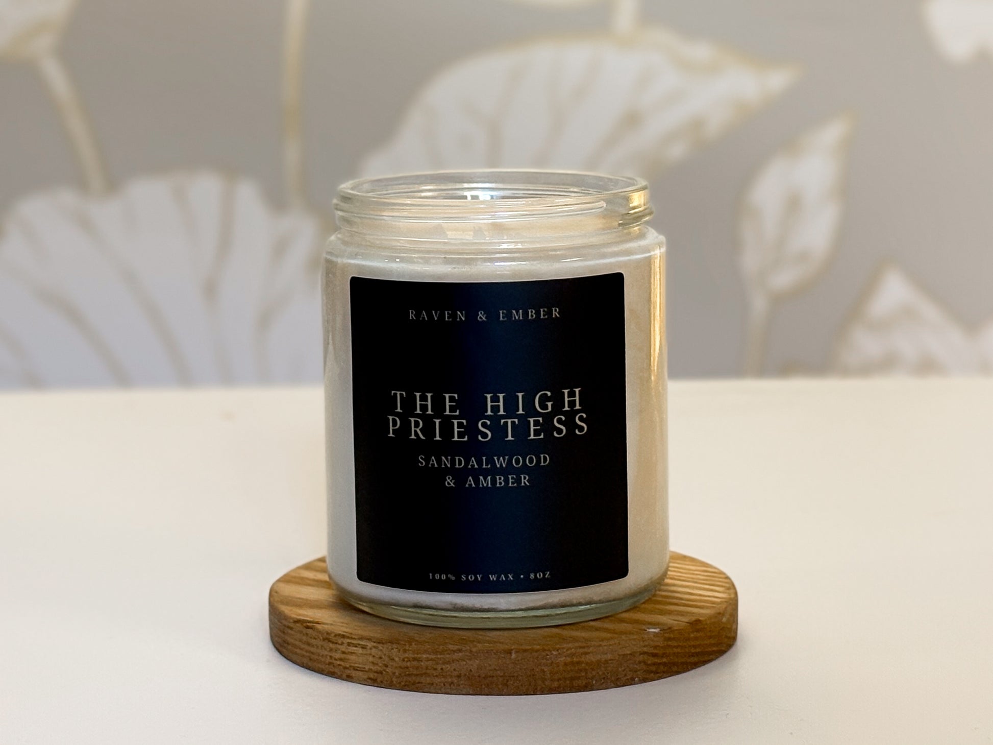Candle jar labeled 'The High Priestess' on a wooden coaster with a neutral background