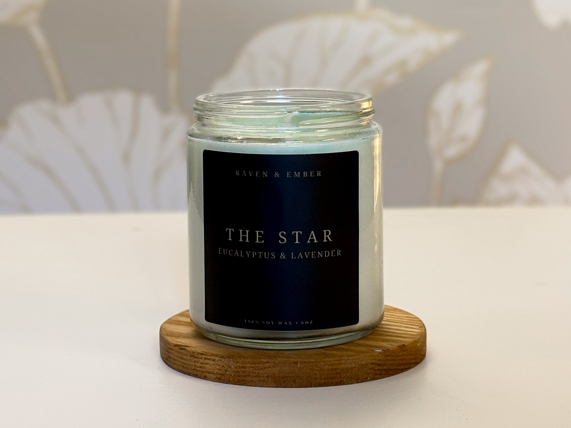 Candle labeled 'The Star' with eucalyptus and lavender on a wooden coaster.
