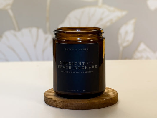 Brown candle jar labeled 'Midnight in the Peach Orchard' on a wooden coaster with a neutral background