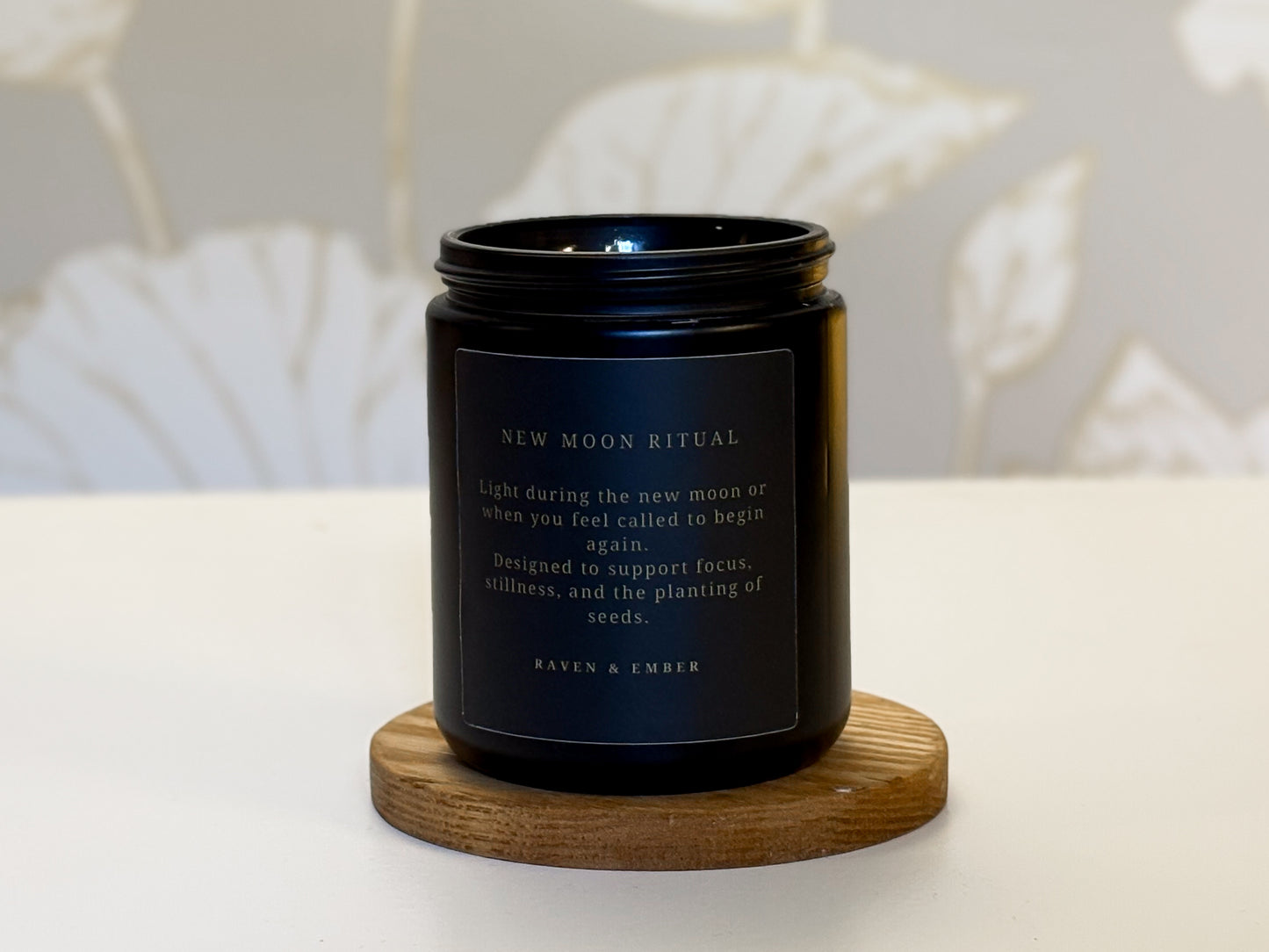 Black candle with a label on a wooden coaster against a neutral background