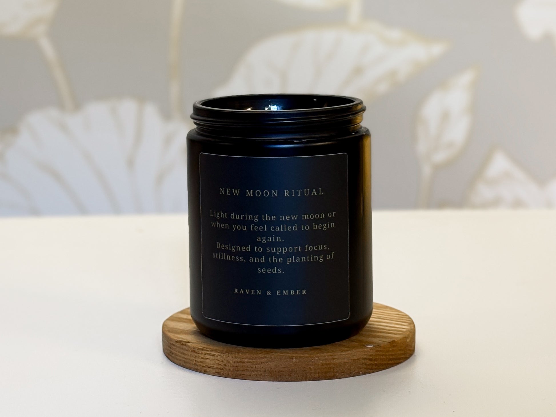 Black candle with a label on a wooden coaster against a neutral background