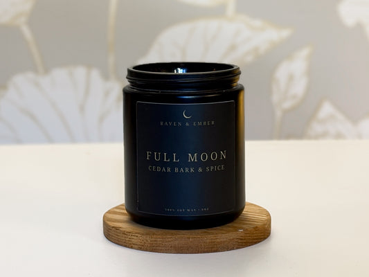 Black candle labeled 'Full Moon' on a wooden coaster with a neutral background