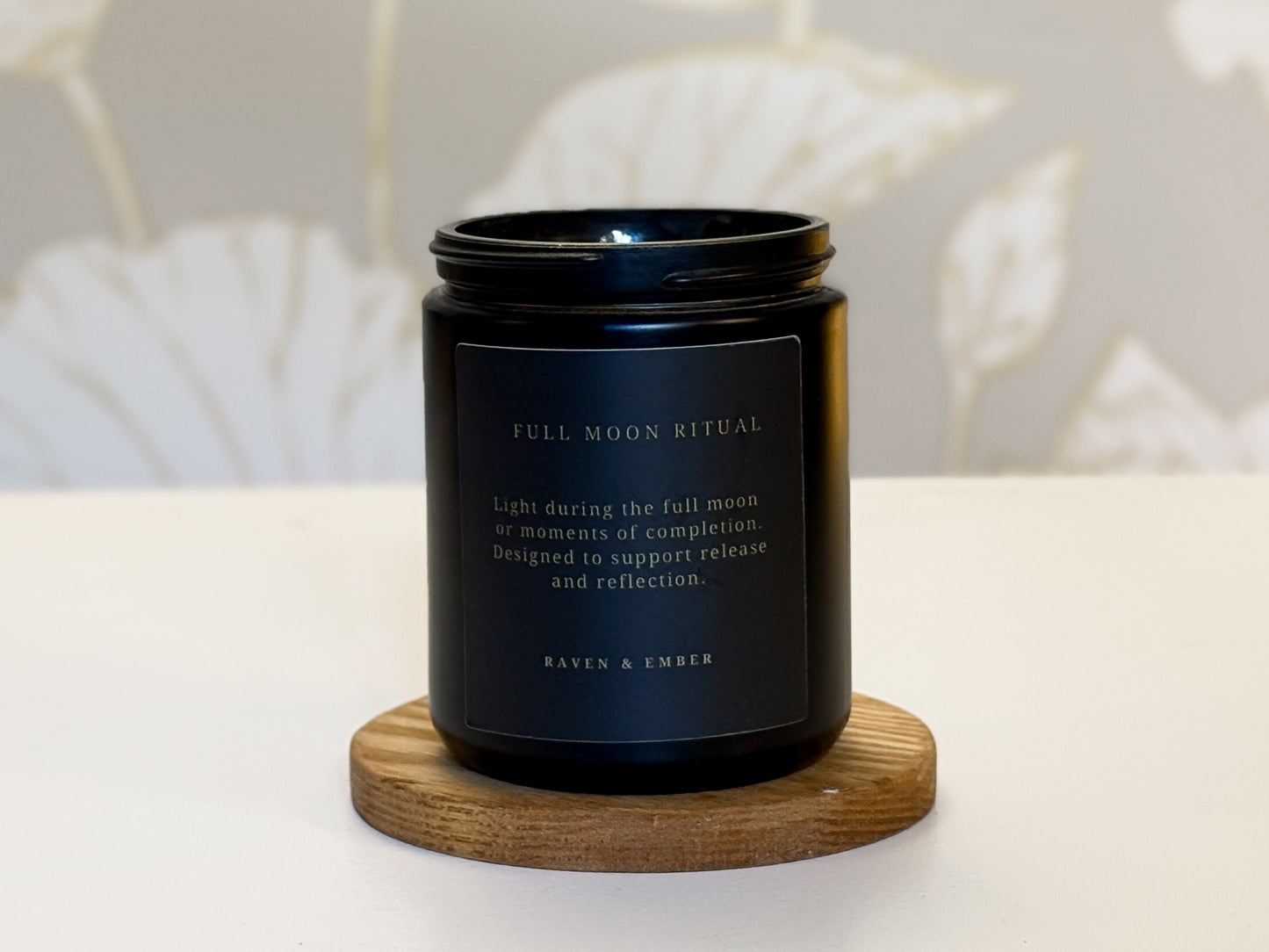 Black candle with a label on a wooden coaster against a neutral background