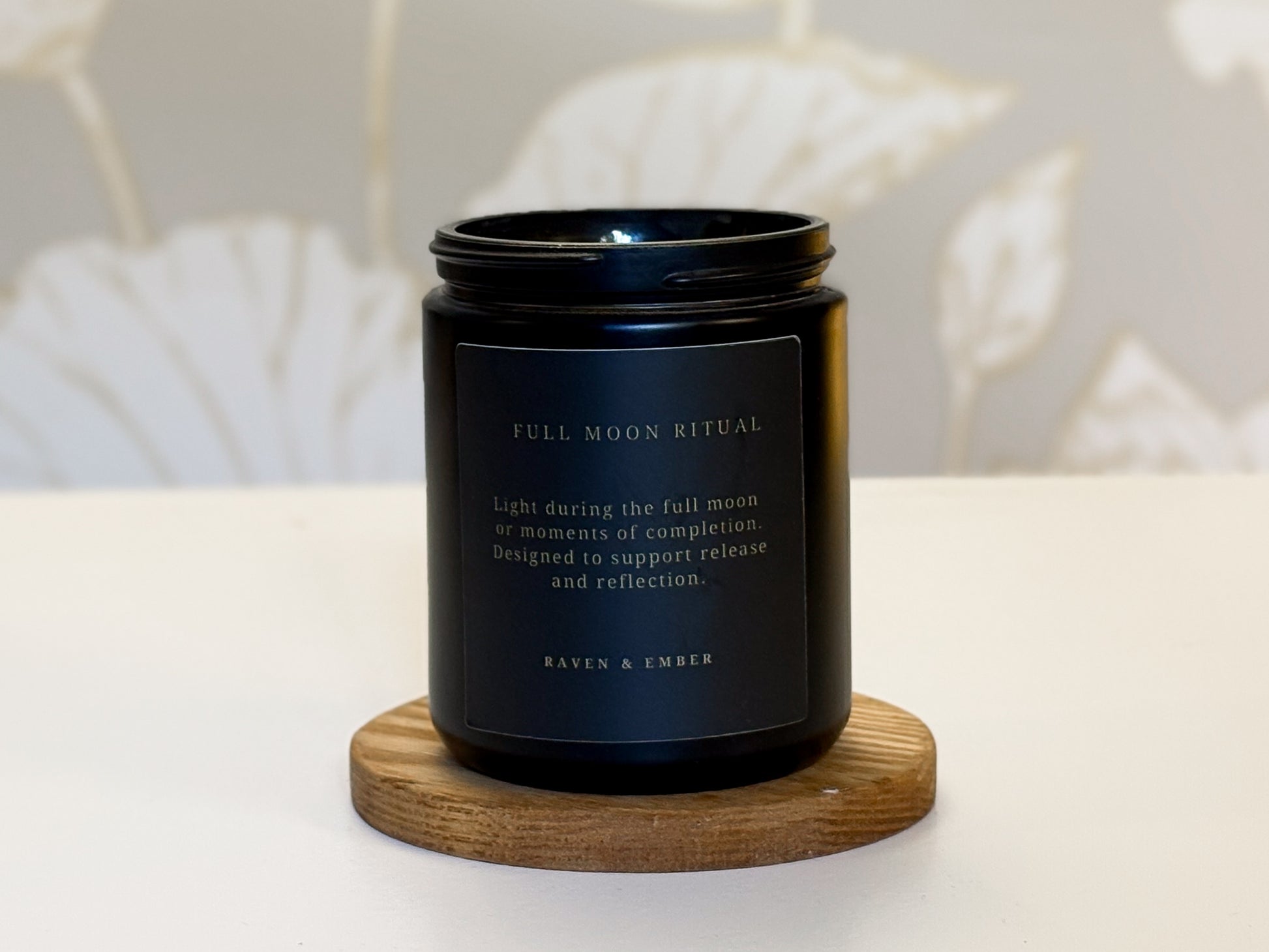 Black candle with a label on a wooden coaster against a neutral background